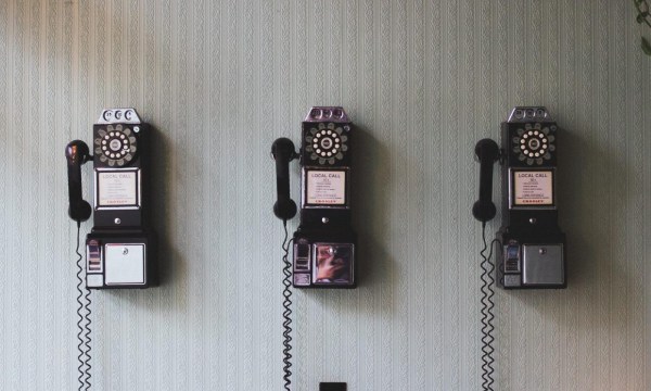Drei Münztelefone mit Wählscheibe hängen an einer Wand